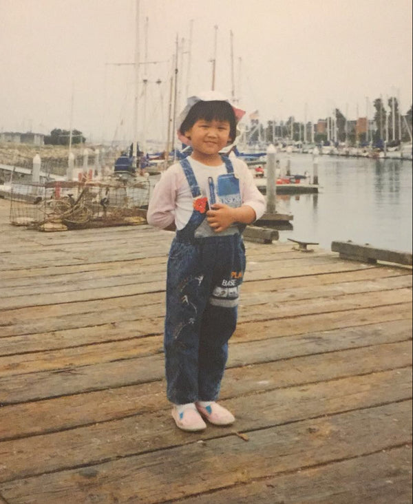 Child standing on a wooden dock by a waterfront with boats in the background